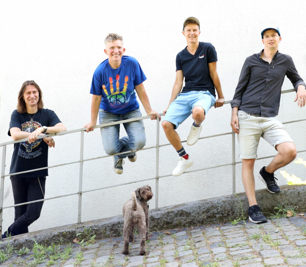 Suli Puschban mit Band: Vier Personen lehnen an einem Geländer, davor steht ein Hund.
