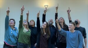 Acht Personen recken ihren rechten Arm in die Höhe und zeigen mit dem Zeigefinger nach oben - das Schlussbild der Tanzchoreographie zu One Billion Rising.